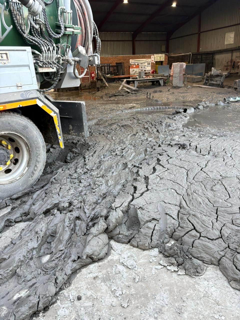 Vacuum tanker equipment beside sludge and a hose on the facility floor