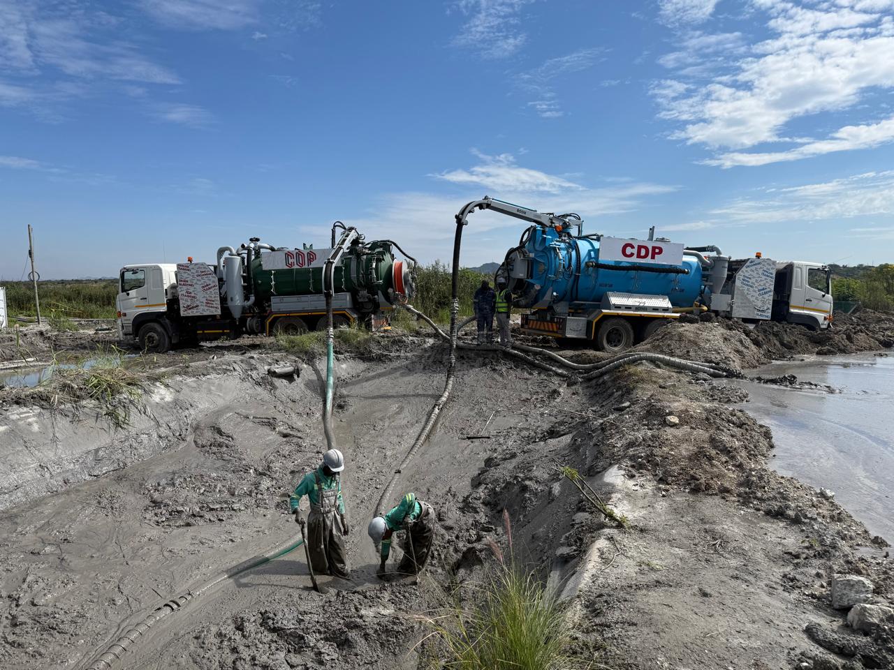 Two CDP vacuum trucks with hoses and workers in protective equipment at a sludge-covered outdoor site